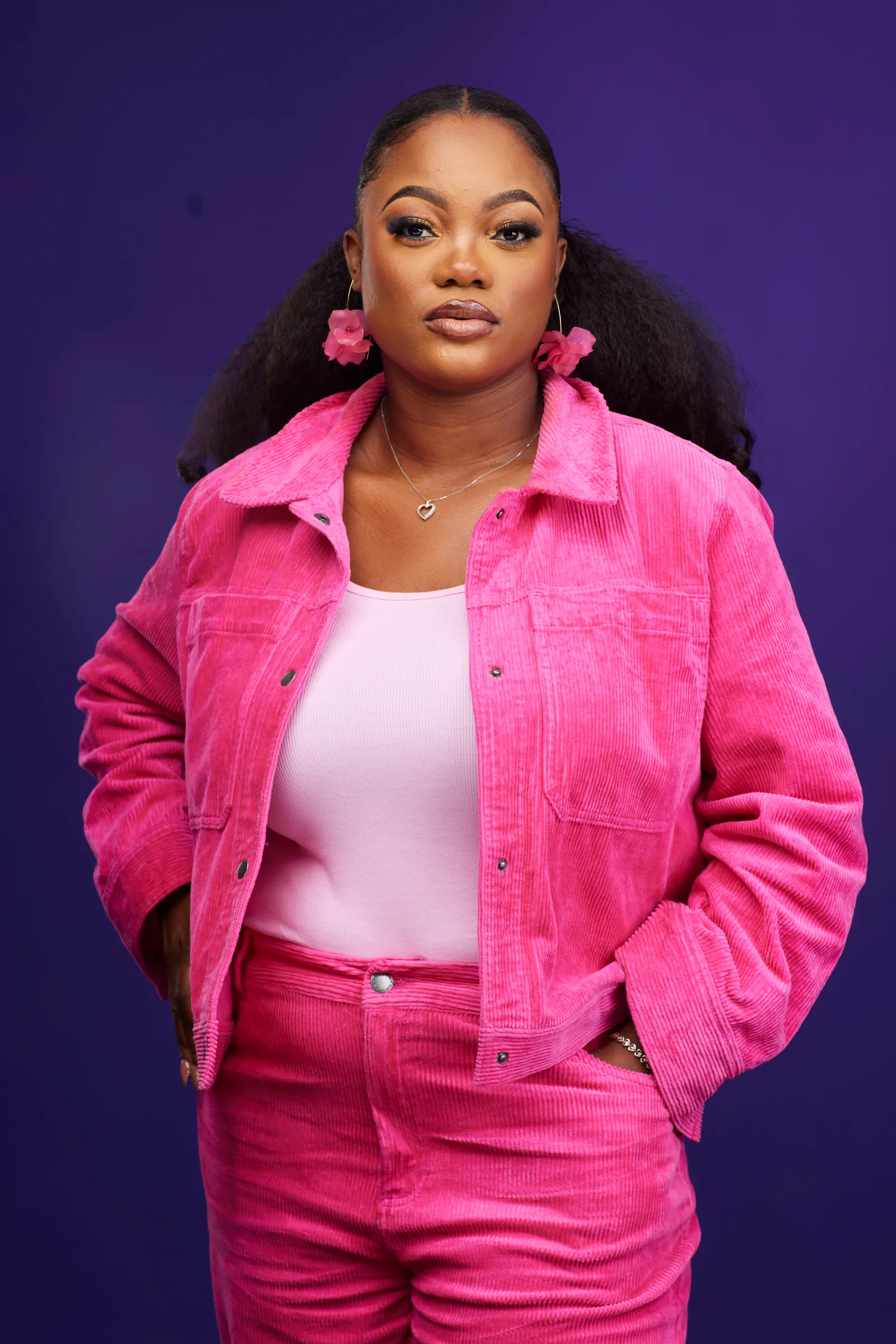 Deborah Lukalu en ensemble de velours rose sur fond violet, face caméra.