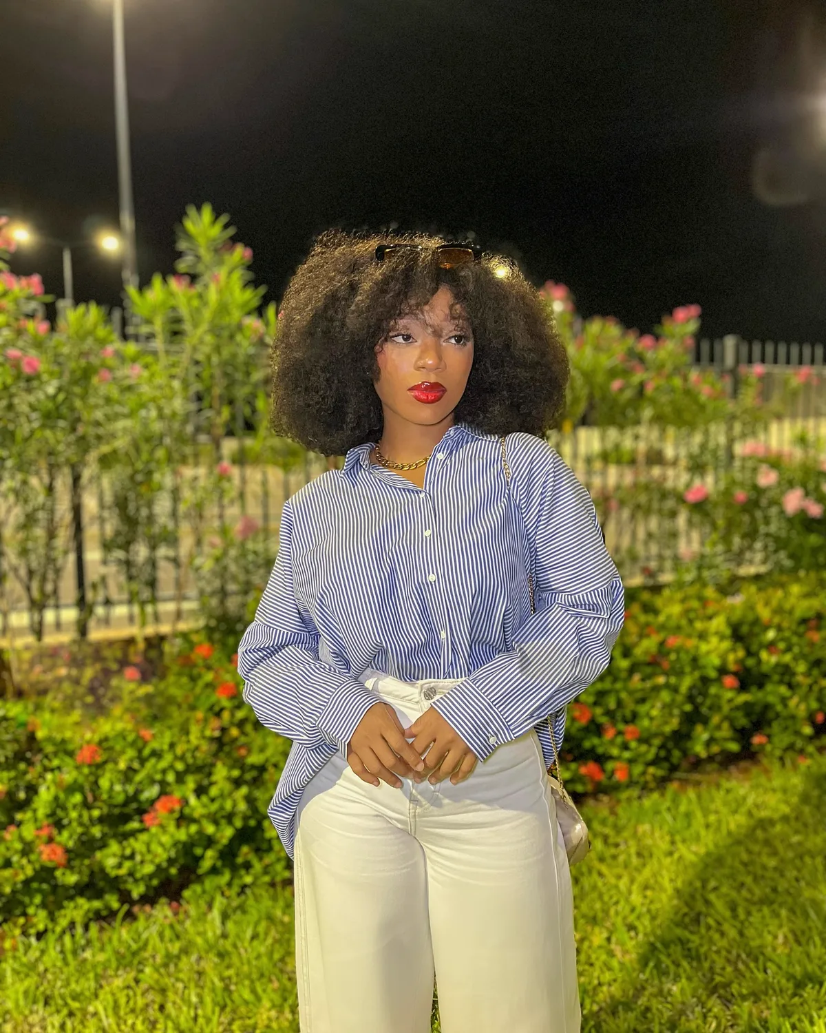 Olyvia de nuit dans un jardin, chemise rayée et pantalon blanc. Photographie réelle.